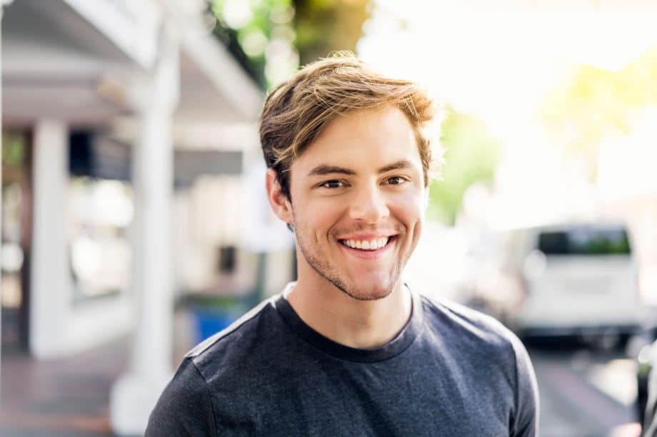 young man standing on sidewalk, smiling